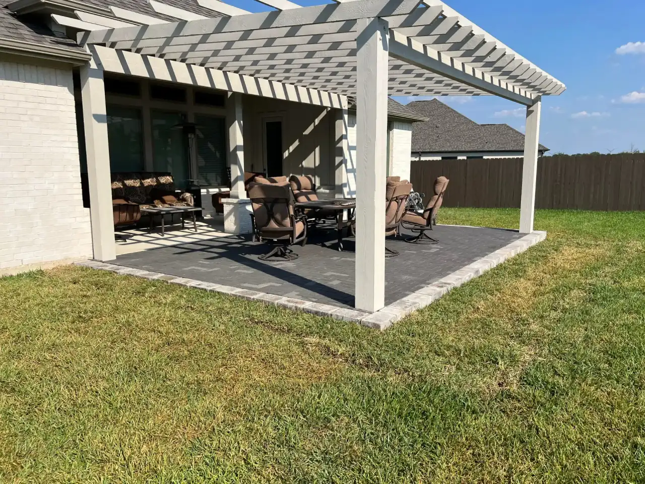 White pergola shading a furnished paver patio off the back of a home