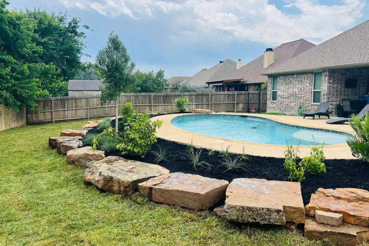 Stacked stone border and new plantings framing a backyard pool