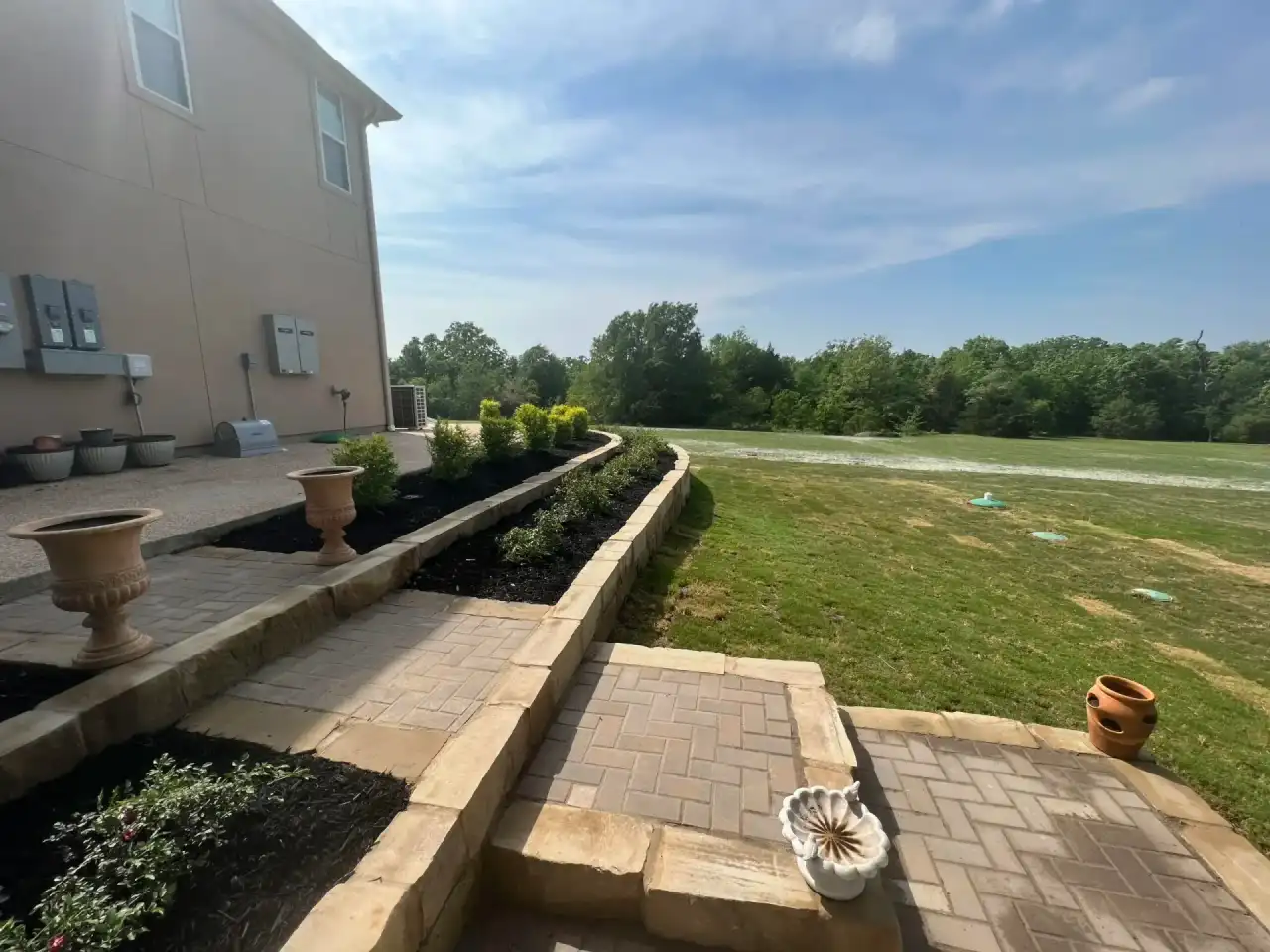 Tiered stone retaining wall holding planted beds beside a paver landing