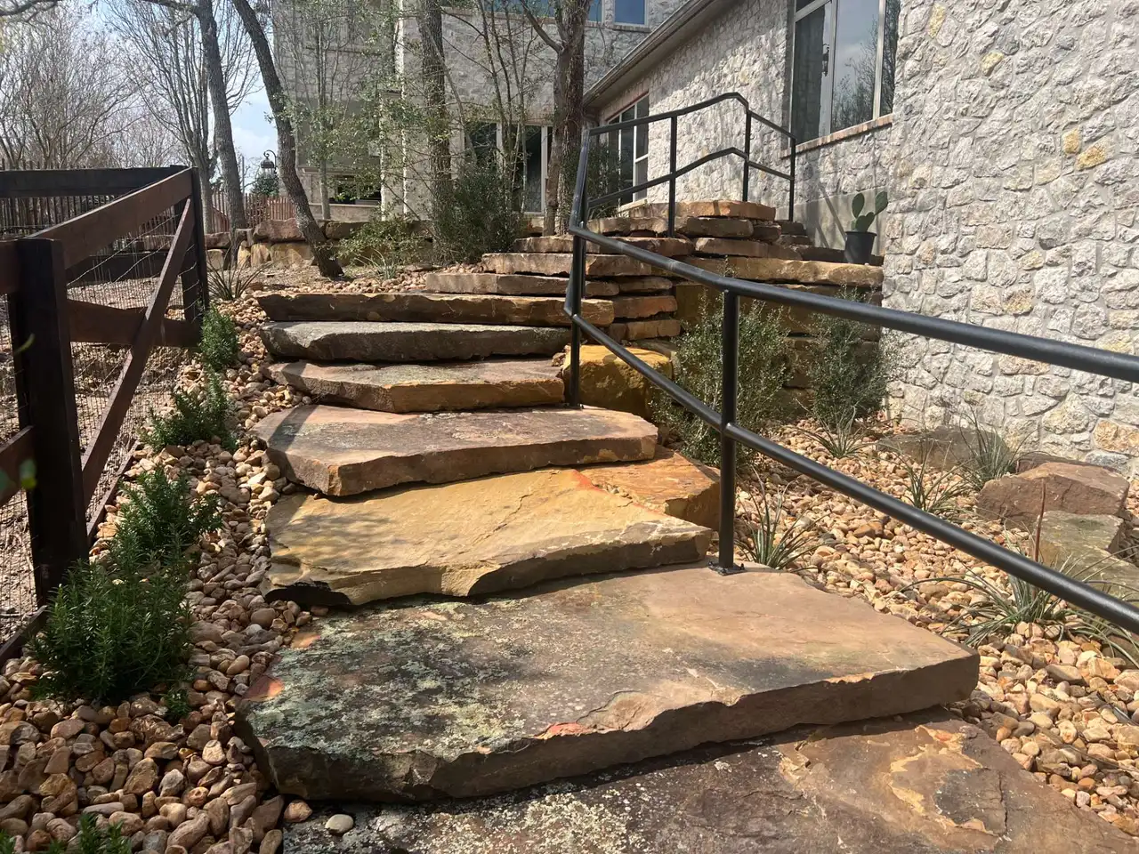 Stone slab steps with a metal handrail rising through a gravel bed