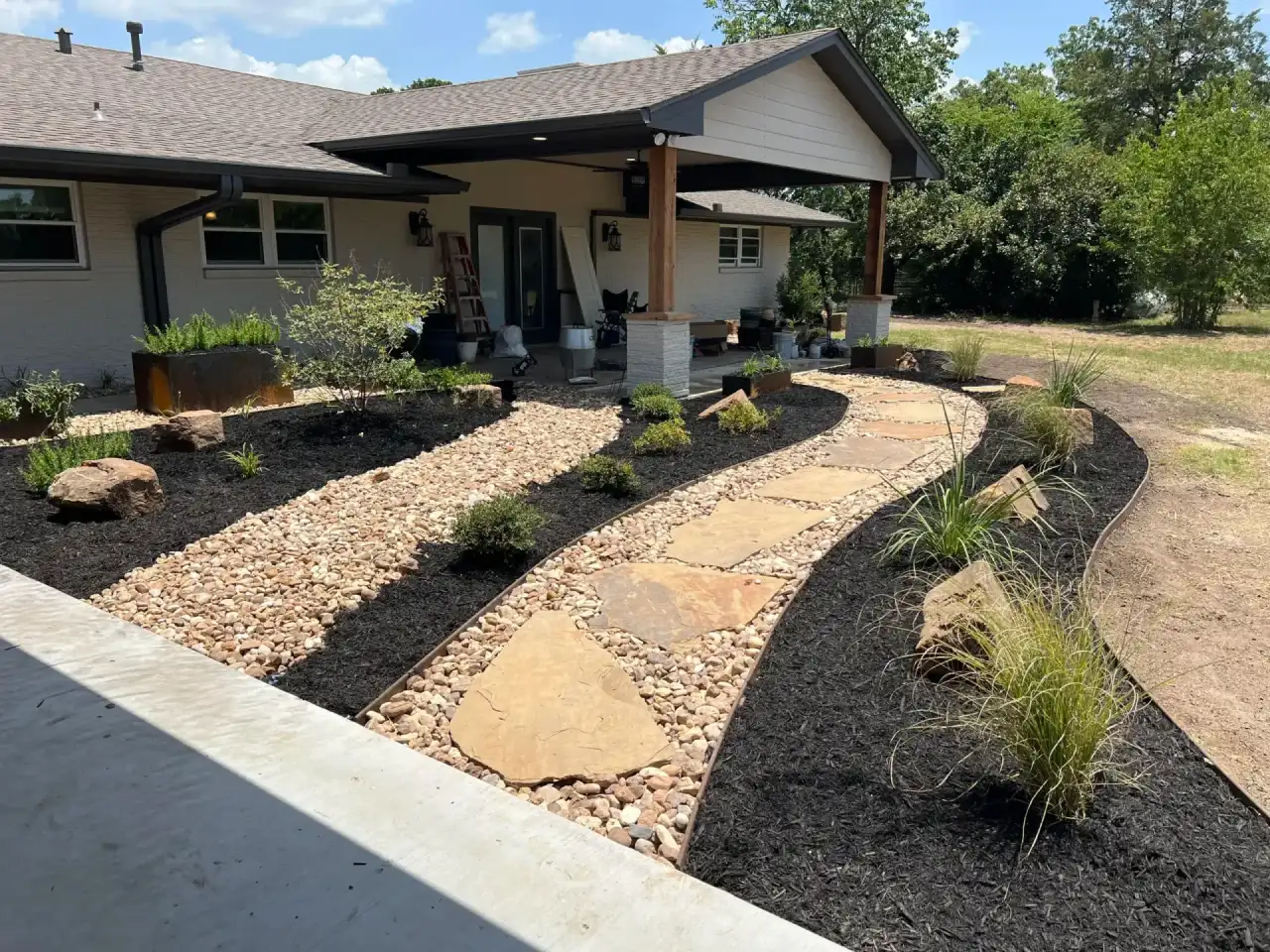 Flagstone walkway set through river rock beds toward a covered porch